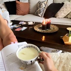 a person sitting on a couch reading a book and holding a cup with liquid in it