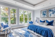 a bedroom with blue and white decor in front of two large windows that look out onto the trees