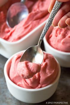 someone spooning out some pink ice cream in small white bowls with silver spoons