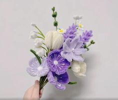 a person holding a bouquet of flowers with purple and white flowers in it's center