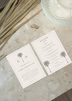 two palm trees are on top of the wedding program and place cards in front of a glass plate