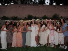 a group of women standing next to each other in front of a brick wall with flowers on their heads