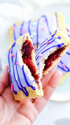 a hand holding a pastry with purple icing and sprinkles