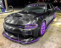 a black car with purple rims parked in front of a gas station at night