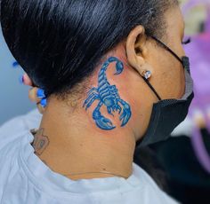 a woman with a blue scorpion tattoo on her neck and behind her ear, wearing a black face mask