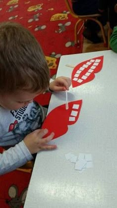 a young boy is making a cutout for a paper boat at a table with other children