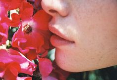 a close up of a woman's face with flowers in the foreground and a bee on her lip