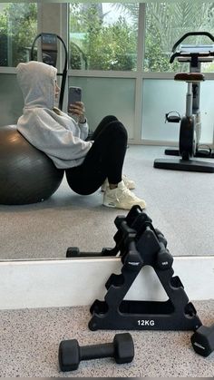 a person sitting on an exercise ball while using a cell phone in a gym area