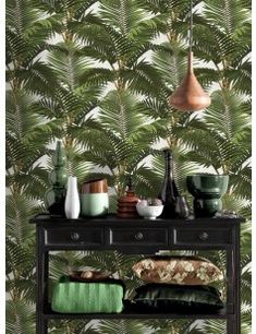 a black table topped with lots of green plants next to a wall covered in palm leaves