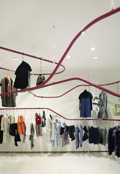 a clothing store with clothes hanging from the ceiling and on display racks in front of them