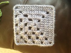 a crocheted square sitting on top of a brown leather bag next to a green flower