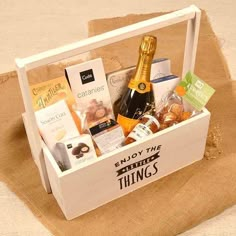 a bottle of champagne and snacks in a white box on a beige cloth covered tablecloth