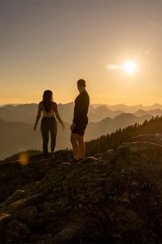 two people standing on top of a mountain at sunset