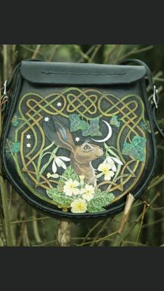 a black purse with an image of a deer and flowers on the front is hanging from a tree