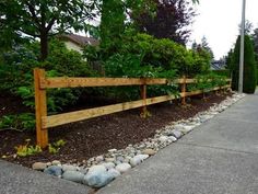 a long wooden fence is lined with rocks and gravel in front of a house on a street