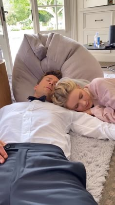 a man and woman laying on the floor in front of a bean bag chair with their arms around each other