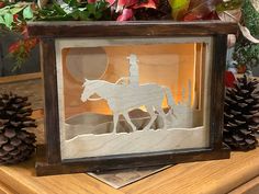 a shadow of a man on a horse in a frame with pine cones and flowers behind it