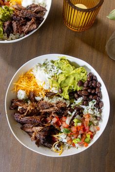 two white plates filled with food on top of a wooden table next to a drink