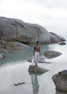 a shirtless man standing on rocks in the water near some large rocks and boulders