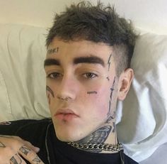 a young man with tattoos on his face and neck is laying in bed looking at the camera