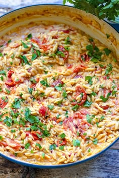 pasta with tomatoes and parsley in a blue dish on a wooden table next to some parsley