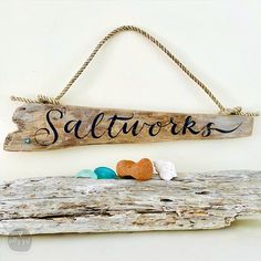 a wooden sign that says sallows hanging on a wall with sea shells and seashells