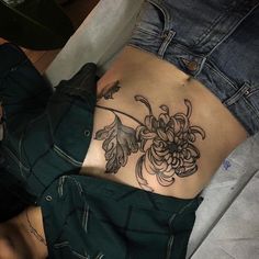 a woman's lower back tattoo with flowers and leaves on her stomach, while she is laying down