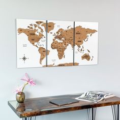 a wooden table topped with a vase filled with flowers next to two framed world maps