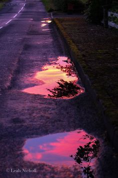 the sky is reflected in some puddles on the side of the road at sunset