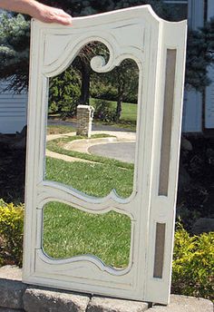 a large white mirror sitting on top of a stone wall next to a lush green field