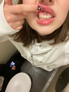 a woman with braces and piercing on her nose standing in front of a toilet