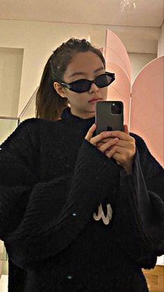 a woman taking a selfie in front of a mirror wearing sunglasses and a black sweater