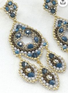 a pair of blue and brown earrings on a white surface with gold trimmings