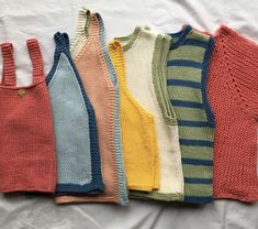 six sweaters are lined up on a white sheet and one is red, yellow, blue, green, orange