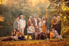 a large group of people posing for a photo in the woods with autumn leaves on the ground