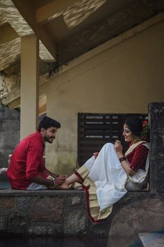 a man sitting next to a woman on top of a stone wall in front of a building