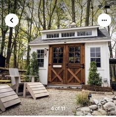 a small white shed with wooden doors in the front yard and steps leading up to it