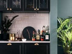 a kitchen with black cabinets and green plants in the corner, along with white tile walls