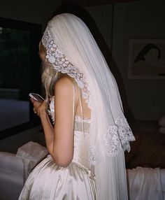 a woman in a wedding dress looking at her cell phone while wearing a white veil