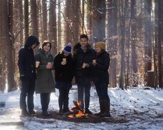 four people standing around a campfire in the woods with their hands on their hips