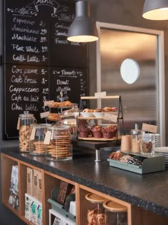 an assortment of pastries and desserts on display at a cafe counter in front of a chalkboard