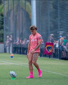 a man in pink shirt kicking a soccer ball on field with people watching from the sidelines