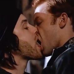 two men are kissing each other while one is wearing a leather jacket and the other has his mouth open