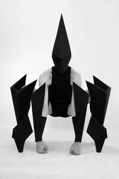 a person sitting on the ground with their legs spread out in front of them, wearing an origami mask