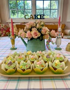 cupcakes are arranged on a table with pink roses in a watering can and candles