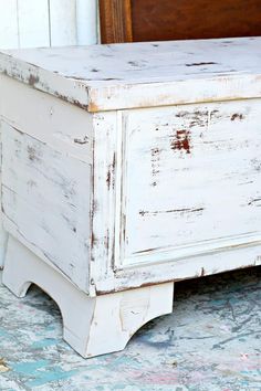 an old white chest with peeling paint on the top and bottom, sitting in front of a bed