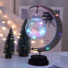 a christmas ornament with lights in the shape of a moon and trees on a table