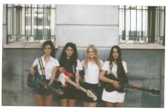 three girls are posing with guitars and holding their guitars in front of a building wall