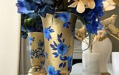 two gold vases with blue and white flowers in them sitting on a table next to a mirror