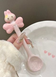 a person holding a pink spoon with a small angel on it's handle next to a white plate